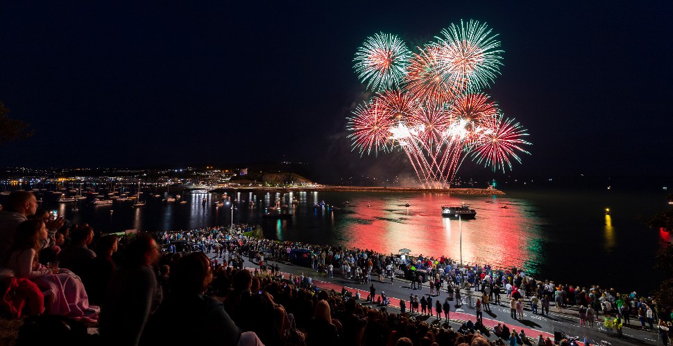 Red and green fireworks over Plymouth Sound with a crowd of people watching  